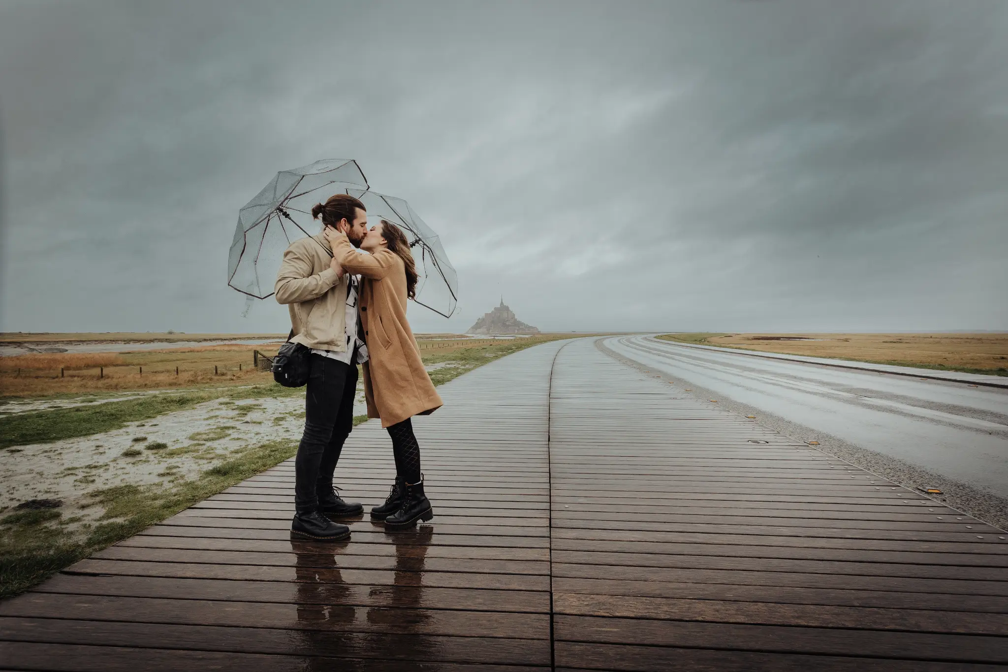 Couple s’embrassant sur la digue du Mont-Saint-Michel avec le monument en arrière-plan — séance photo demande en mariage
