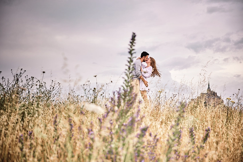 Couple s'embrassant dans les prés sauvages du Mont-Saint-Michel après la demande en mariage — séance photo fiançailles Normandie