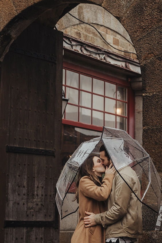 Couple s'embrassant sous un parapluie transparent dans les ruelles du Mont-Saint-Michel après la demande en mariage