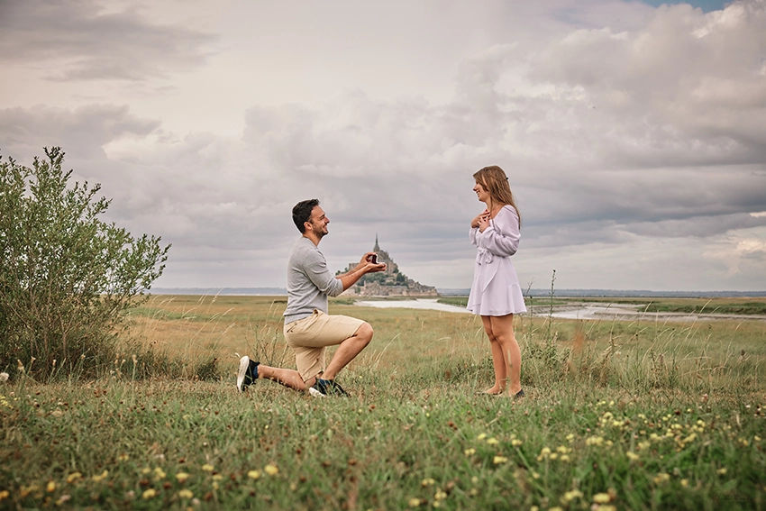 Demande en mariage dans les prés du Mont-Saint-Michel — homme à genoux offrant la bague, photographe demande en mariage Normandie