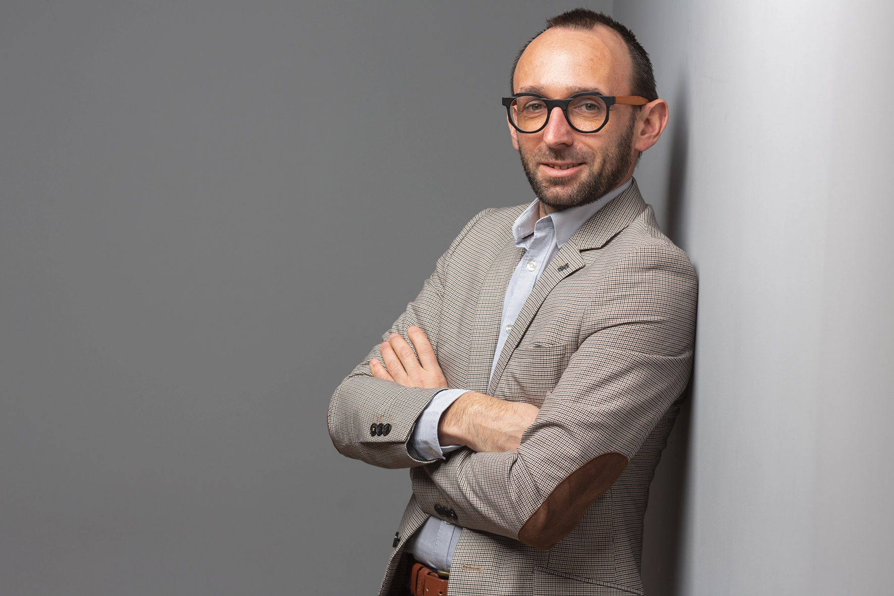 Portrait corporate homme veste à carreaux bras croisés adossé au mur, sourire confiant — Photographe portrait professionnel Dol-de-Bretagne, Saint-Malo, Ille-et-Vilaine