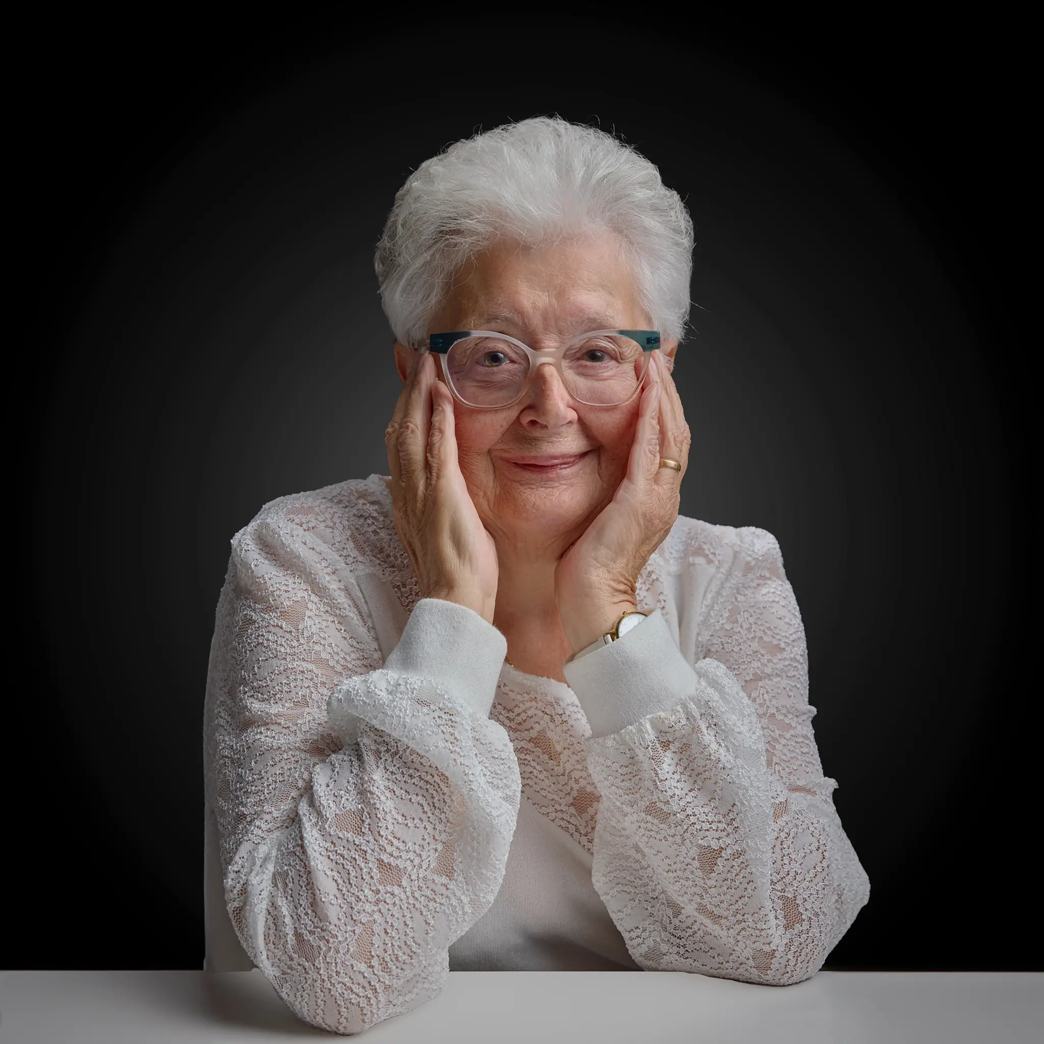 Portrait femme âgée cheveux blancs lunettes bleues, mains sur les joues fond noir — Photographe portrait Dol-de-Bretagne, Combourg, Ille-et-Vilaine